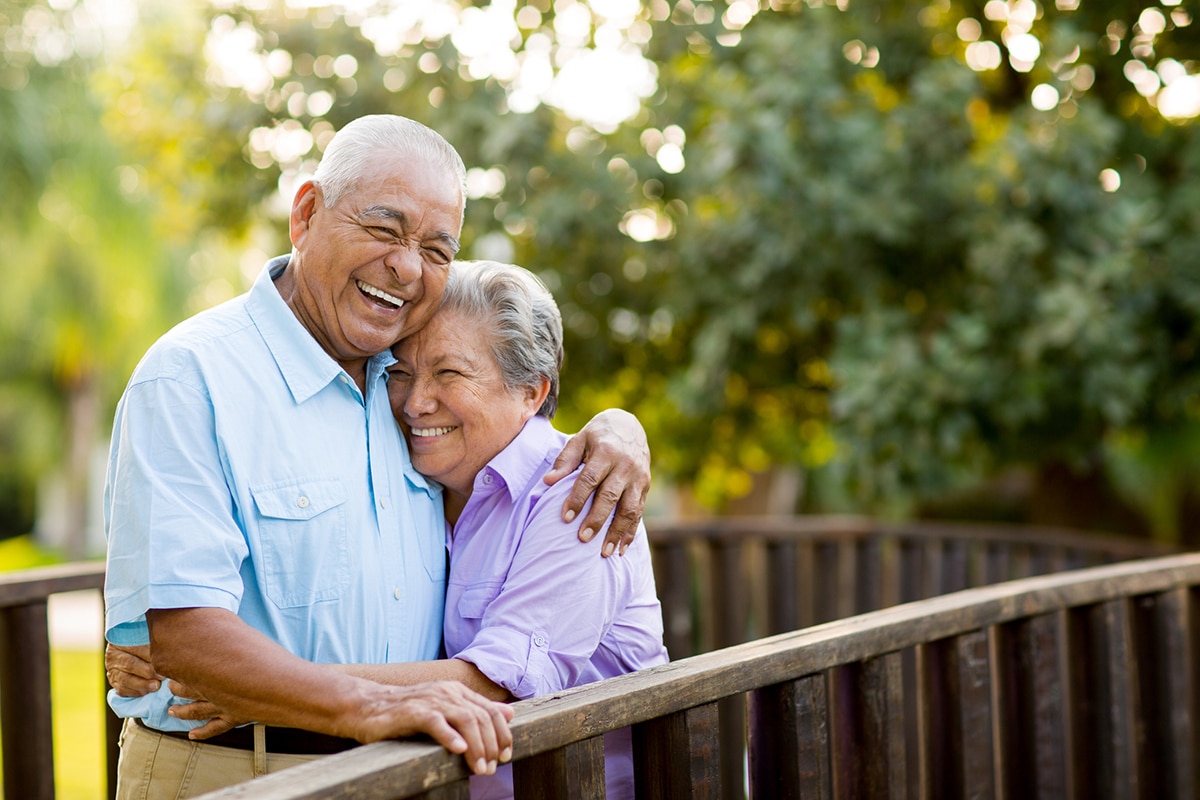 older couple standing on wooden bridge, hugging