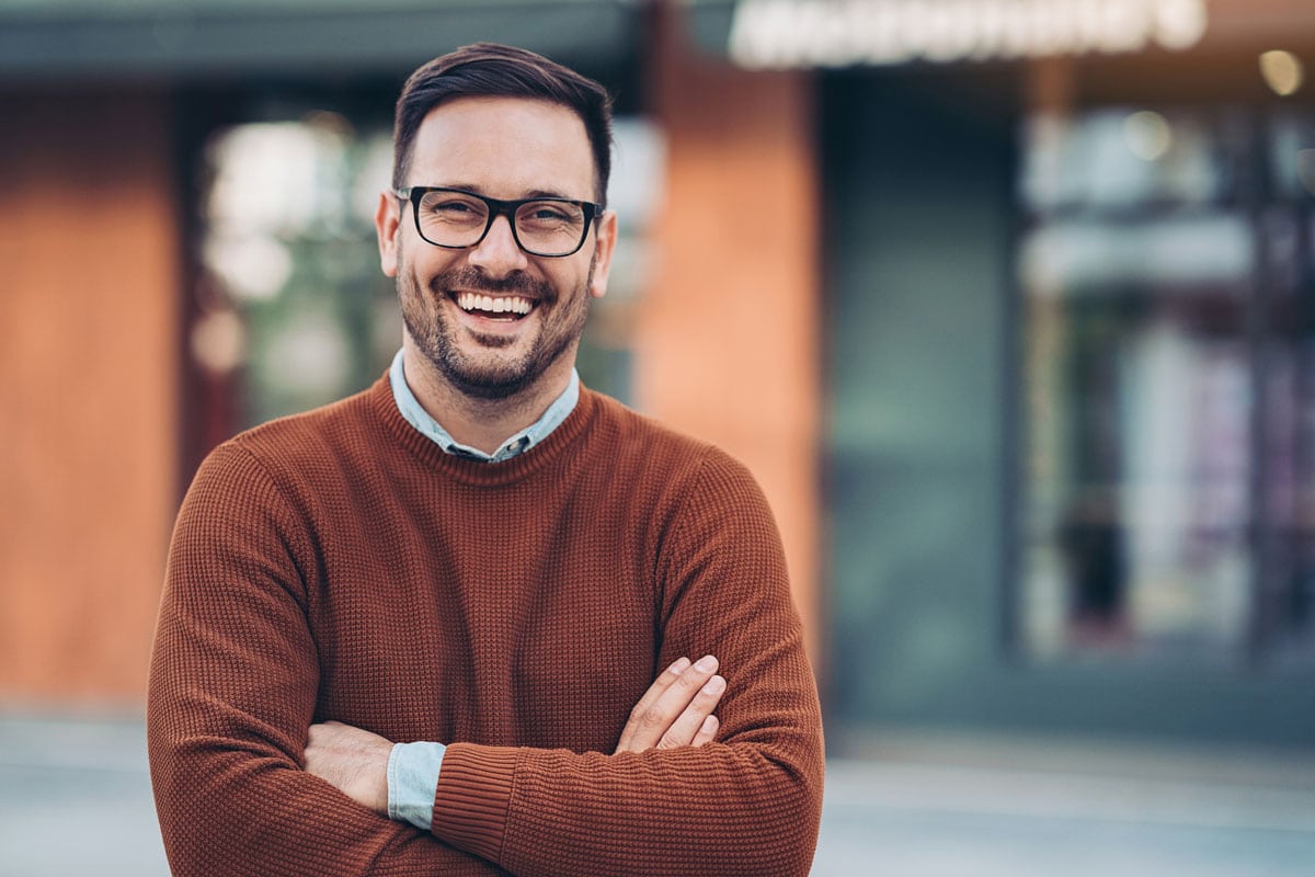 smiling man with arms crossing standing outside