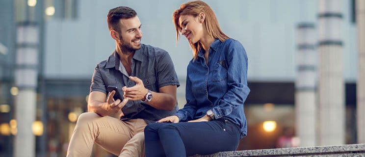 man and woman sitting along sidewalk while they look at his phone