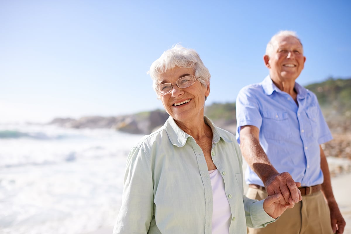 older couple holding hands walking along the beach