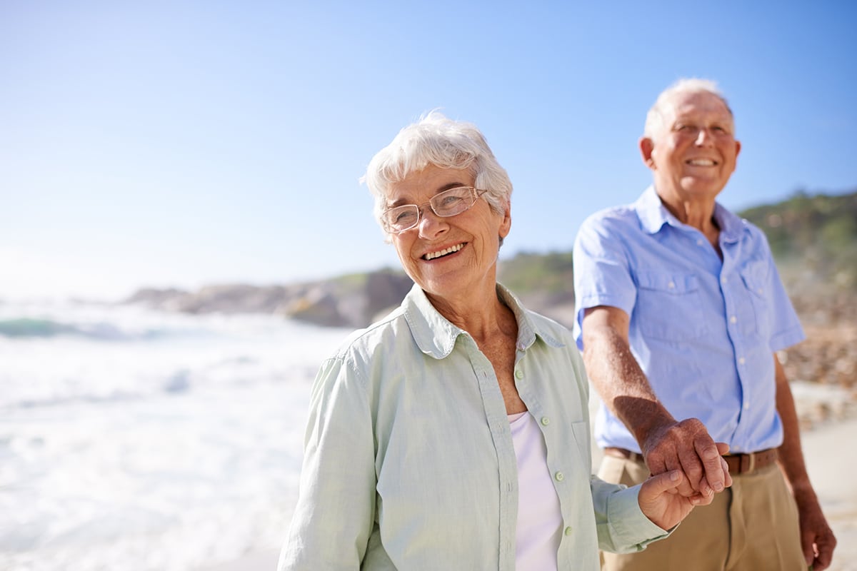 older couple holding hands walking along the beach