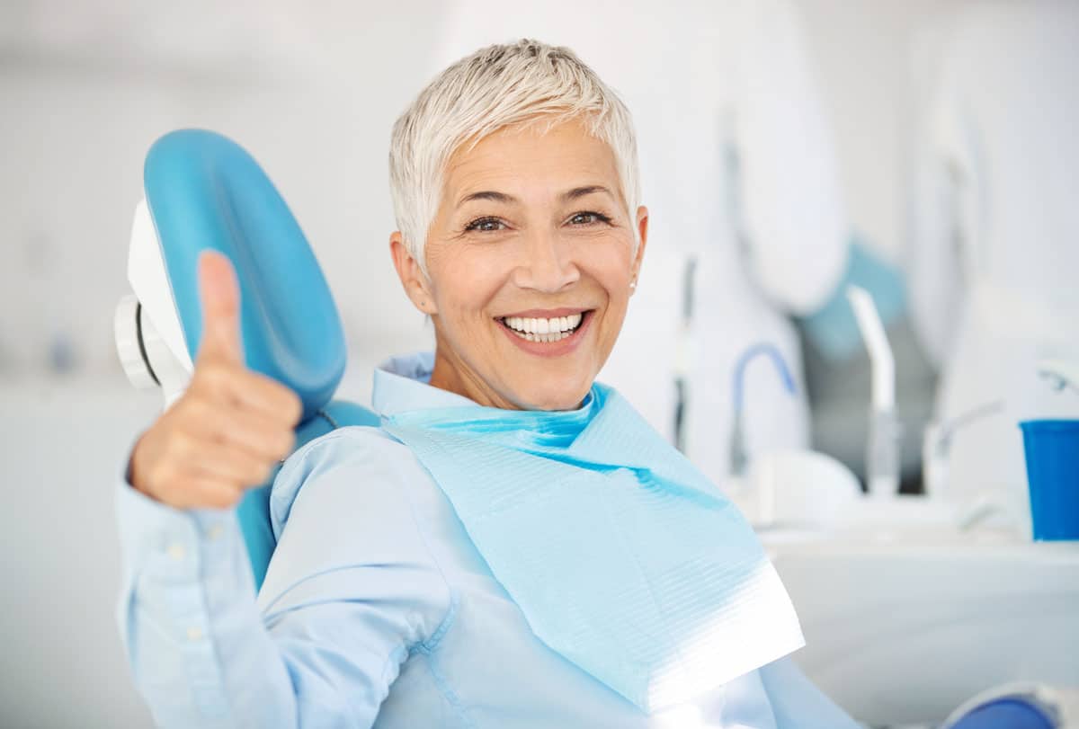 older woman in dental chair signaling with thumbs up
